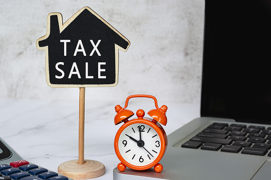 Sign saying, "tax sale" next to a clock, signifying a tax delinquent sale on distressed properties.