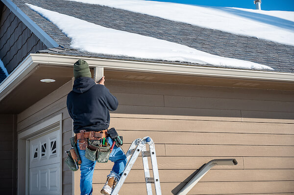 contractor on a ladder fixing gutters on home exterior