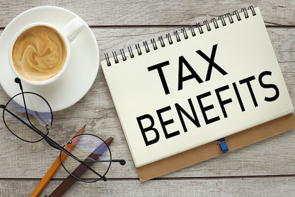 Notebook on table with the phrase, "tax benefits" written on it, next to coffee